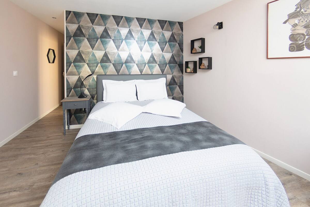 A modern bedroom with a geometric-patterned headboard, a bedside table with a lamp, and a framed artwork on the wall.