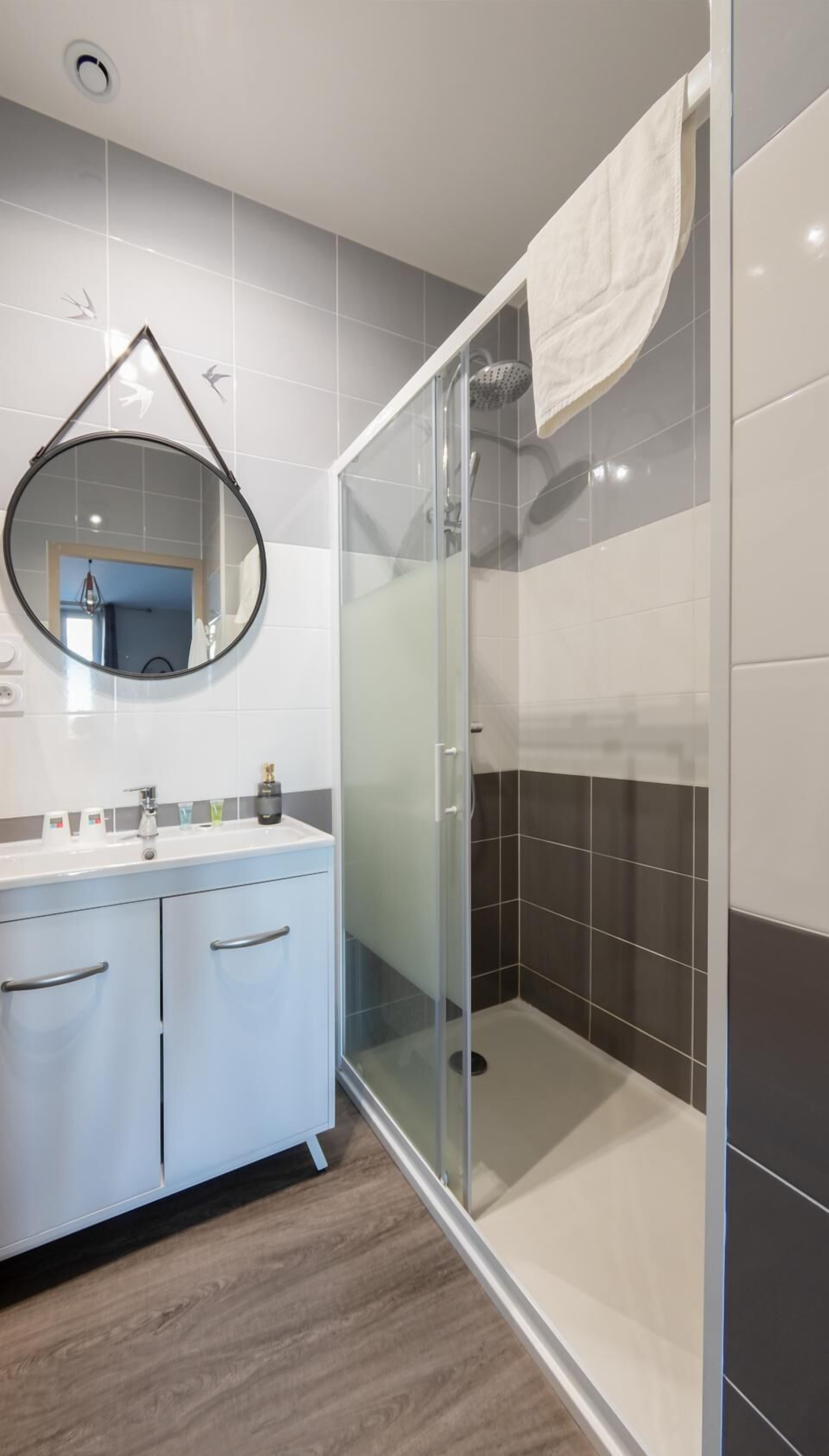 A modern bathroom with a glass-enclosed shower, a vanity with a mirror, and a tiled floor.