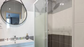 A modern bathroom with a glass-enclosed shower, a vanity with a mirror, and a tiled floor.