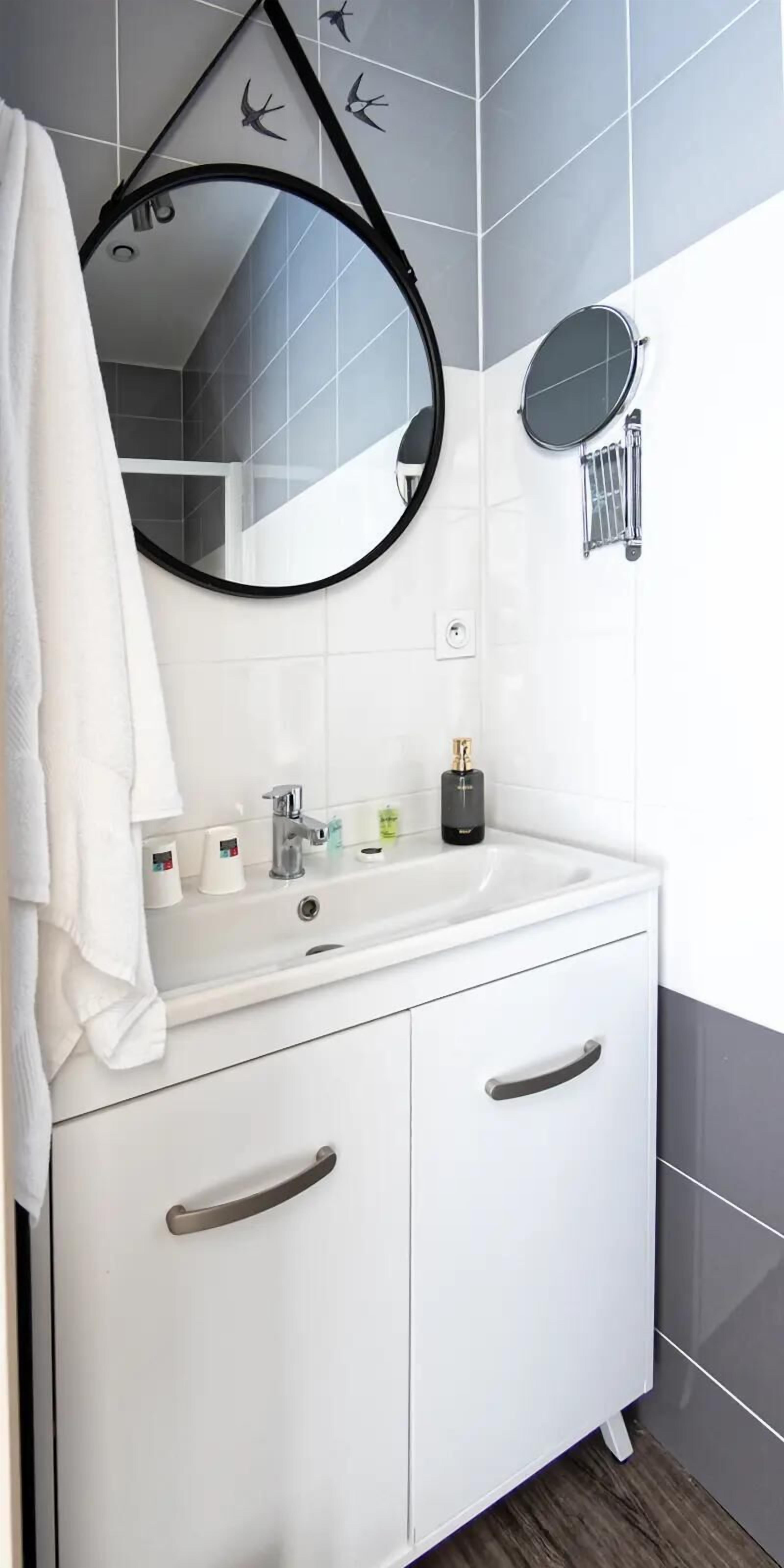 Une salle de bain avec un meuble-lavabo blanc, un miroir rond et une serviette accrochée au mur.