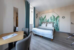 Quarto de hotel com cama, escrivaninha, cadeira e parede com padrão de folhagem.