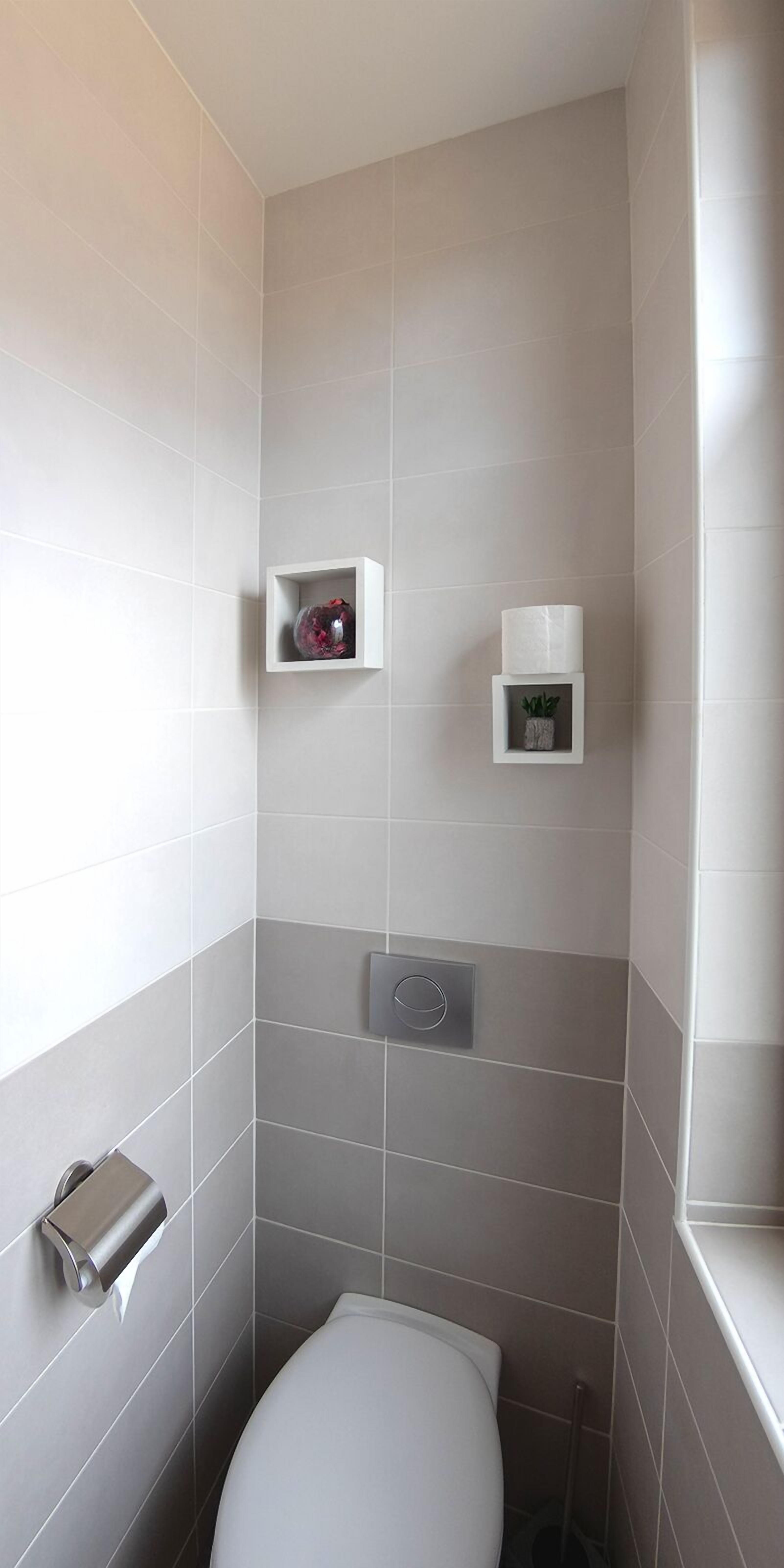 A bathroom with a toilet, a hand dryer, and two small shelves with a decorative item and a plant.
