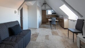 A modern loft apartment with a high ceiling, exposed beams, a kitchenette, a dining area, and a living space with a patterned sofa. - Le Relais de la Poste (Gourdon)