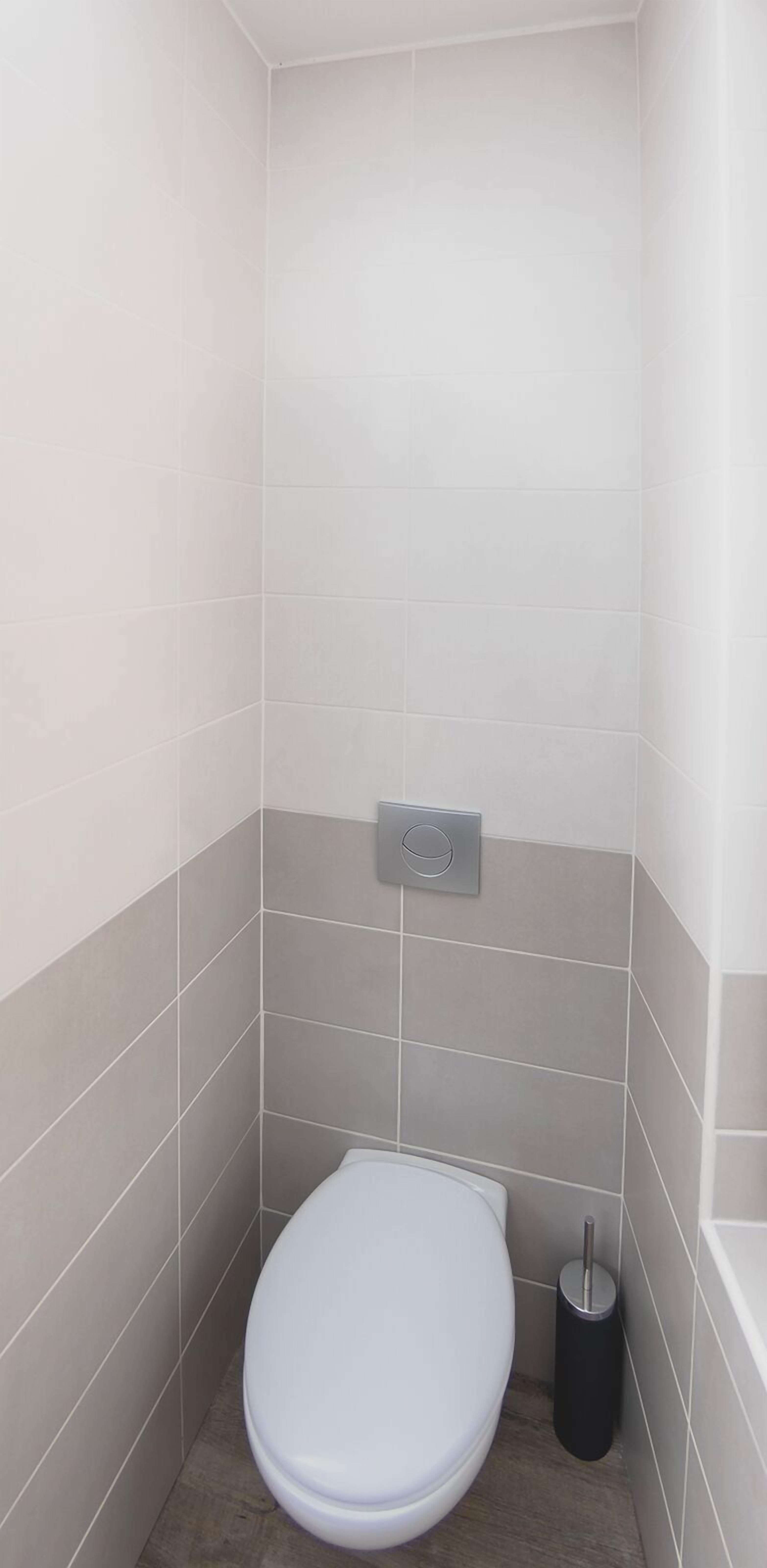 Un baño pequeño y moderno con inodoro, un tirador para la descarga y un cubo de basura.