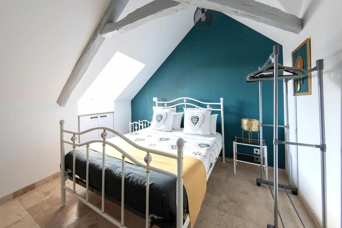 A bedroom with a sloped ceiling, a bed with a white metal frame, a teal accent wall, and a skylight.