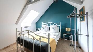 Ein Schlafzimmer mit schrägen Wänden, einem Bett mit weißem Metallgestell, einer Türkis-farbenen Akzentwand und einem Oberlicht.