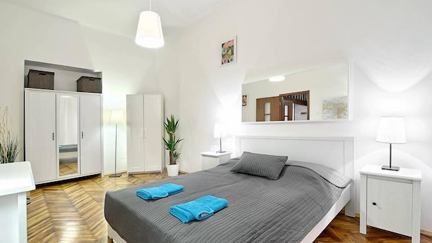 A modern bedroom with a large bed, white wardrobe, bedside tables, and a potted plant.