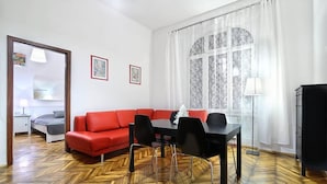A modern living room with a red sofa, a black dining table, and a herringbone wood floor.