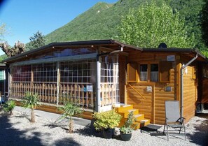 Una casetta di legno con ampie finestre, un piccolo portico e una sedia all'esterno.