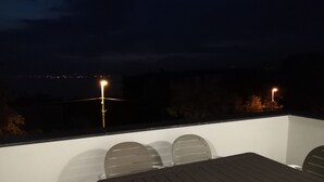 Un patio al aire libre con una mesa y sillas, vista del paisaje urbano de noche y farolas.