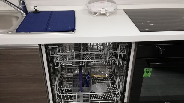 Un lavavajillas abierto con un tapete azul encima, un escurreplatos en su interior y un panel de control con varias opciones.