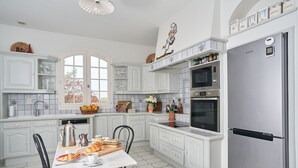 A kitchen with white cabinets, a stainless steel refrigerator, and a dining area with a table and chairs.