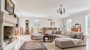 A spacious living room with a fireplace, a large sofa, a coffee table, and a chandelier.
