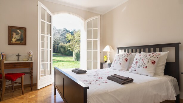 A bedroom with a large bed, a desk, and an open door leading to a garden.