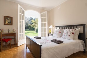 Ein Schlafzimmer mit einem großen Bett, einem Schreibtisch und einer offenen Tür, die in einen Garten führt.