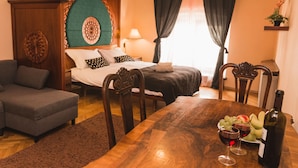 A bedroom with a bed, a wooden headboard, a nightstand, a bedside table, a lamp, a dresser, a grey sofa, a wooden dining table with a bottle of wine, glasses, and a fruit plate. - Filin Apartment (Kraków)