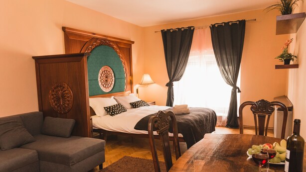 A bedroom with a bed, a wooden headboard, a nightstand, a bedside table, and a window with curtains. - Filin Apartment (Kraków)