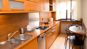 A kitchen with wooden cabinets, a stainless steel sink, a dishwasher, a stove, and a dining area with a table and chairs. - Filin Apartment (Kraków)