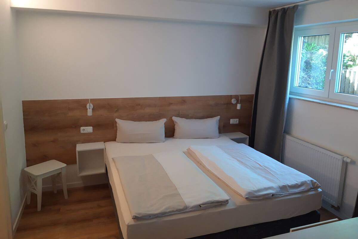 A neatly made bed with a wooden headboard, two bedside tables, and a window with curtains.