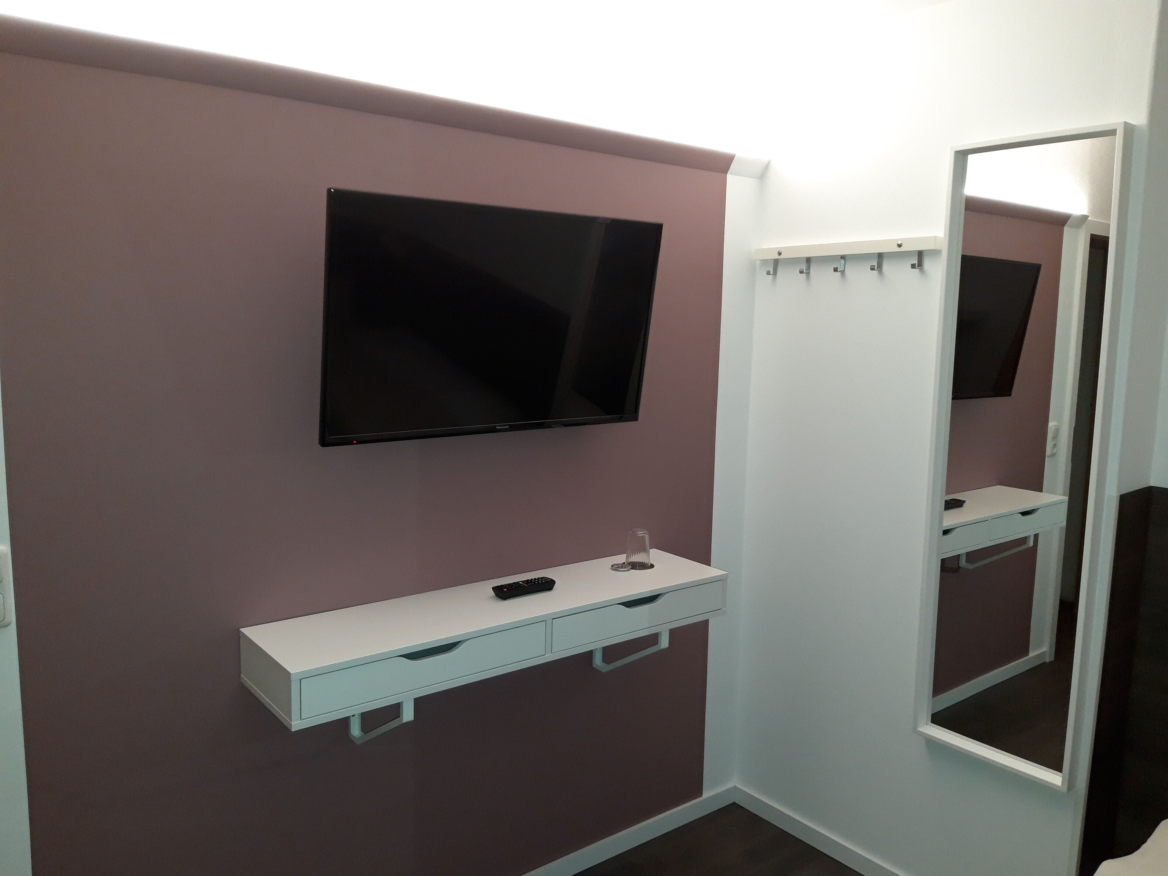 Un bagno moderno con una TV a schermo piatto montata al muro, un mobile vanitario bianco con specchio e un pavimento marrone scuro.