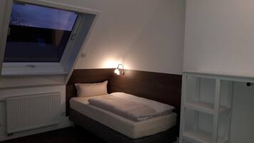 Un dormitorio con cama, mesita de noche, ventana y lámpara fijada a la pared.