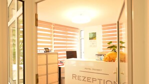 A reception area with a desk, a computer, a calendar, and a plant. - Hotel Weinert (Neubrandenburg)