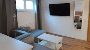 A modern living room with a sofa, a small table, a flat-screen TV, and a window with curtains. - Hotel Weinert (Neubrandenburg)
