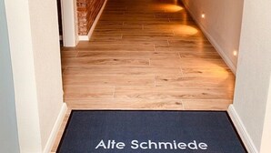 Een gang met houten vloer en een zwarte deurmat met de tekst 'Alte Schmiede'.