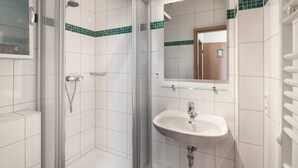 Une salle de bain avec une douche à parois de verre, un lavabo avec un miroir au-dessus et des murs recouverts de carreaux blancs.