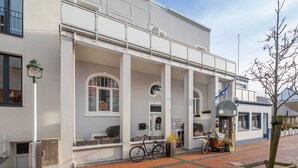 Un bâtiment blanc avec un porche abrité, un vélo et une voiture ancienne garés à l’extérieur.