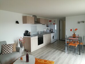 A modern kitchen with a built-in oven, microwave, and washing machine. There is a dining area with a table and chairs, and a living room with a sofa and a coffee table.