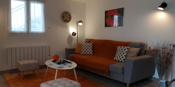 A modern living room with a sofa, ottoman, and a table with a red apple and books.