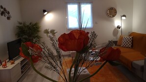 A living room with a sofa, a coffee table with a vase of flowers, a television, and a plant.