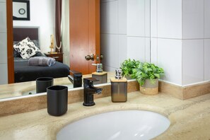 A bathroom with a sink, two black mugs, a black faucet, a potted plant, and a mirror reflecting a bed with a pillow. - Apartment Full Equiped Whit A/C. In The Heart Of Santiago, Chile! (Santiago)