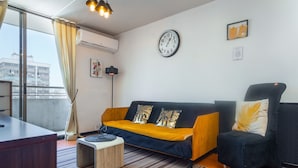 Uma sala de estar moderna com sofá, poltrona, mesa de centro e uma janela grande com cortinas.