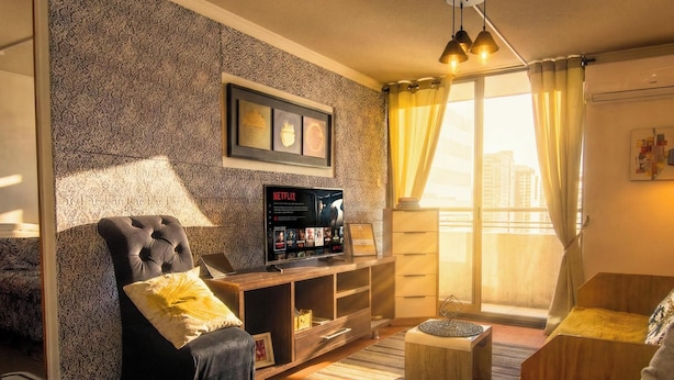 Sala de estar com sofá, poltrona, televisão e janela com cortinas.