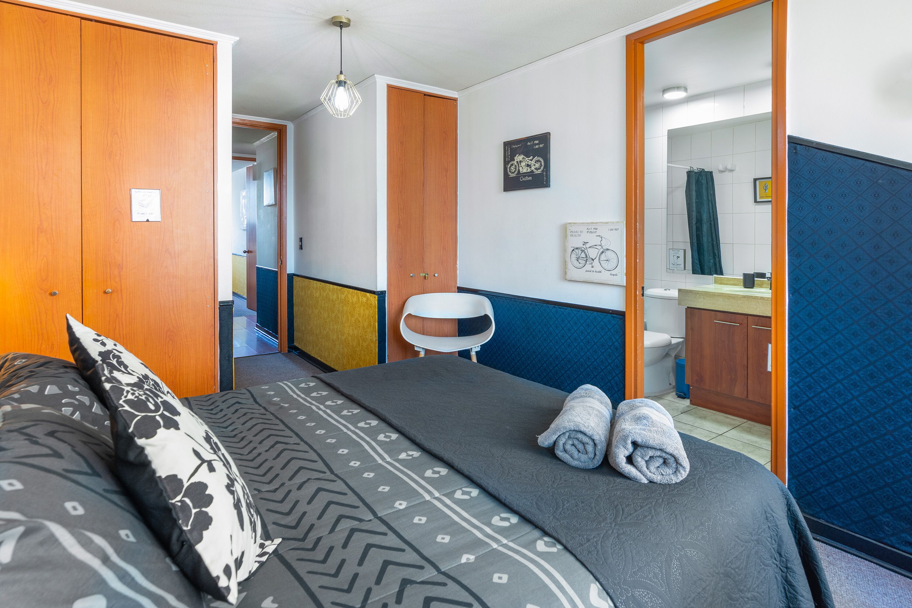 A hotel room with a bed, a chair, a bathroom visible through an open door, and a framed picture on the wall.