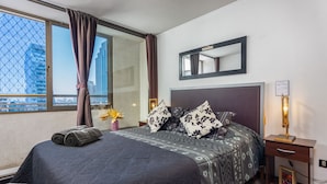 Quarto de hotel com uma cama grande, mesa de cabeceira com abajur, espelho e janela com cortinas.