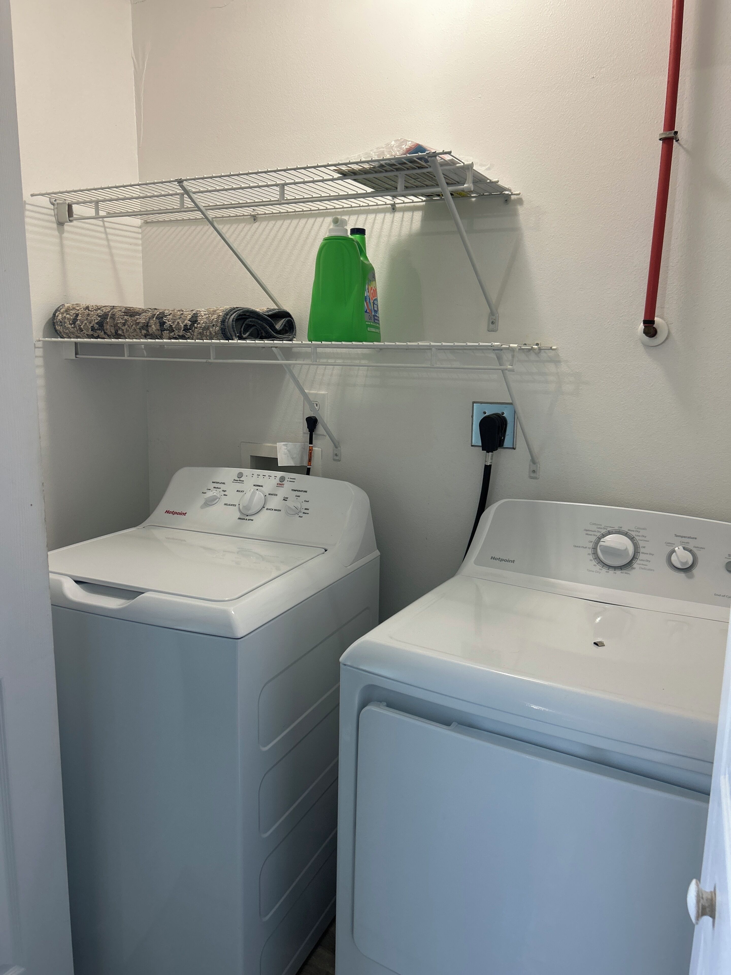 A laundry area with two washing machines, a drying rack, and a green detergent bottle.