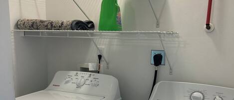 A laundry area with two washing machines, a drying rack, and a green detergent bottle.