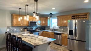 Una cocina moderna con armarios de madera, una isla grande con taburetes de bar, electrodomésticos de acero inoxidable e iluminación colgante.