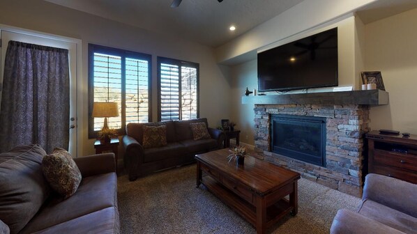 A living room with a fireplace, a sofa, a coffee table, and a television mounted above the fireplace. - Tee Time Golf Course View! (Washington)