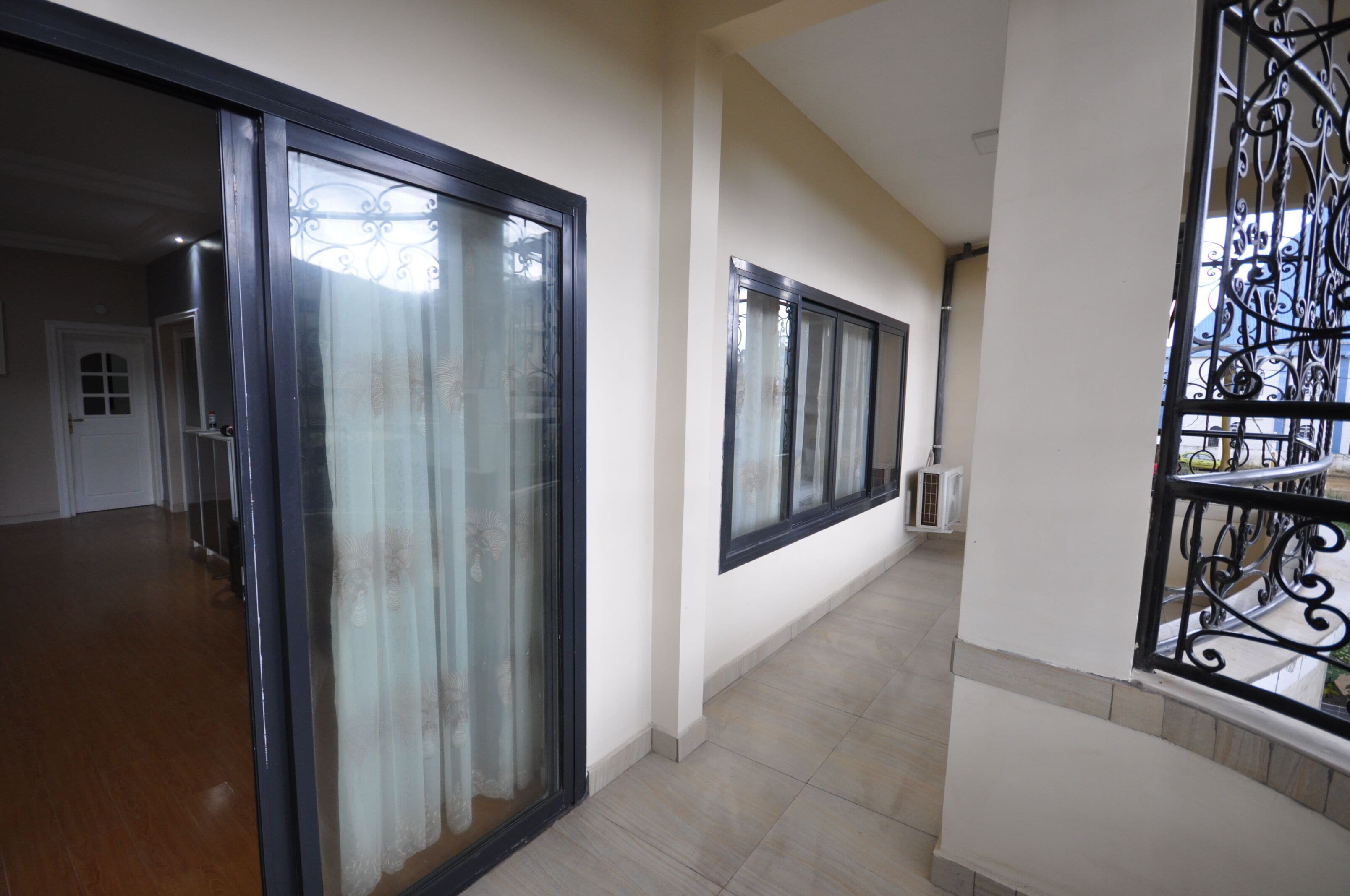 A hallway with a glass door, a black metal railing, and a tiled floor.