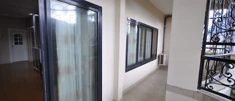 A hallway with a glass door, a black metal railing, and a tiled floor.