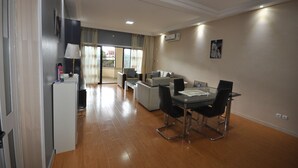A modern living room with a dining area, a sofa set, a coffee table, and a TV. - Line-Residence (Douala)