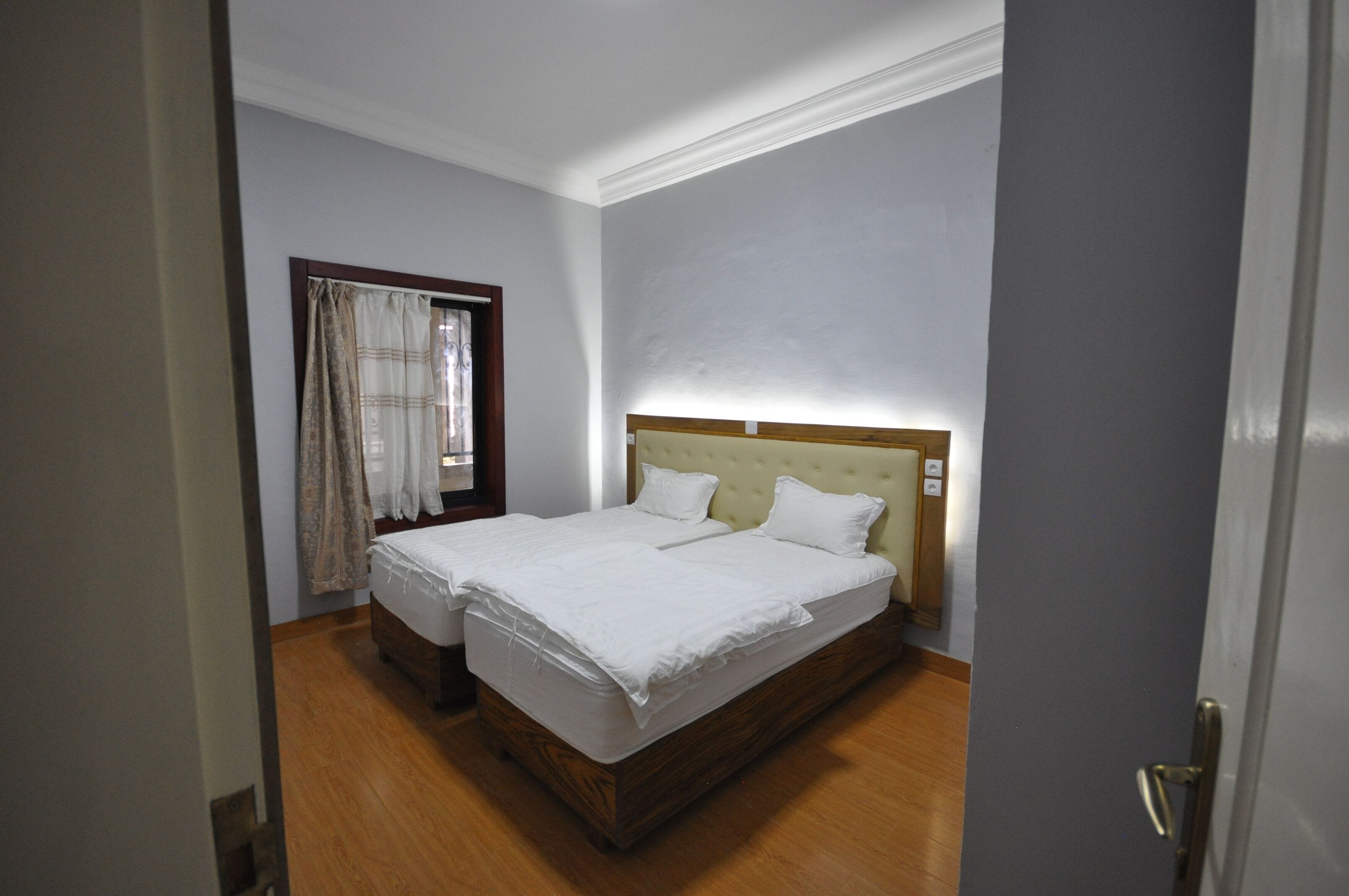 A bedroom with two single beds, wooden flooring, a window with curtains, and a door.
