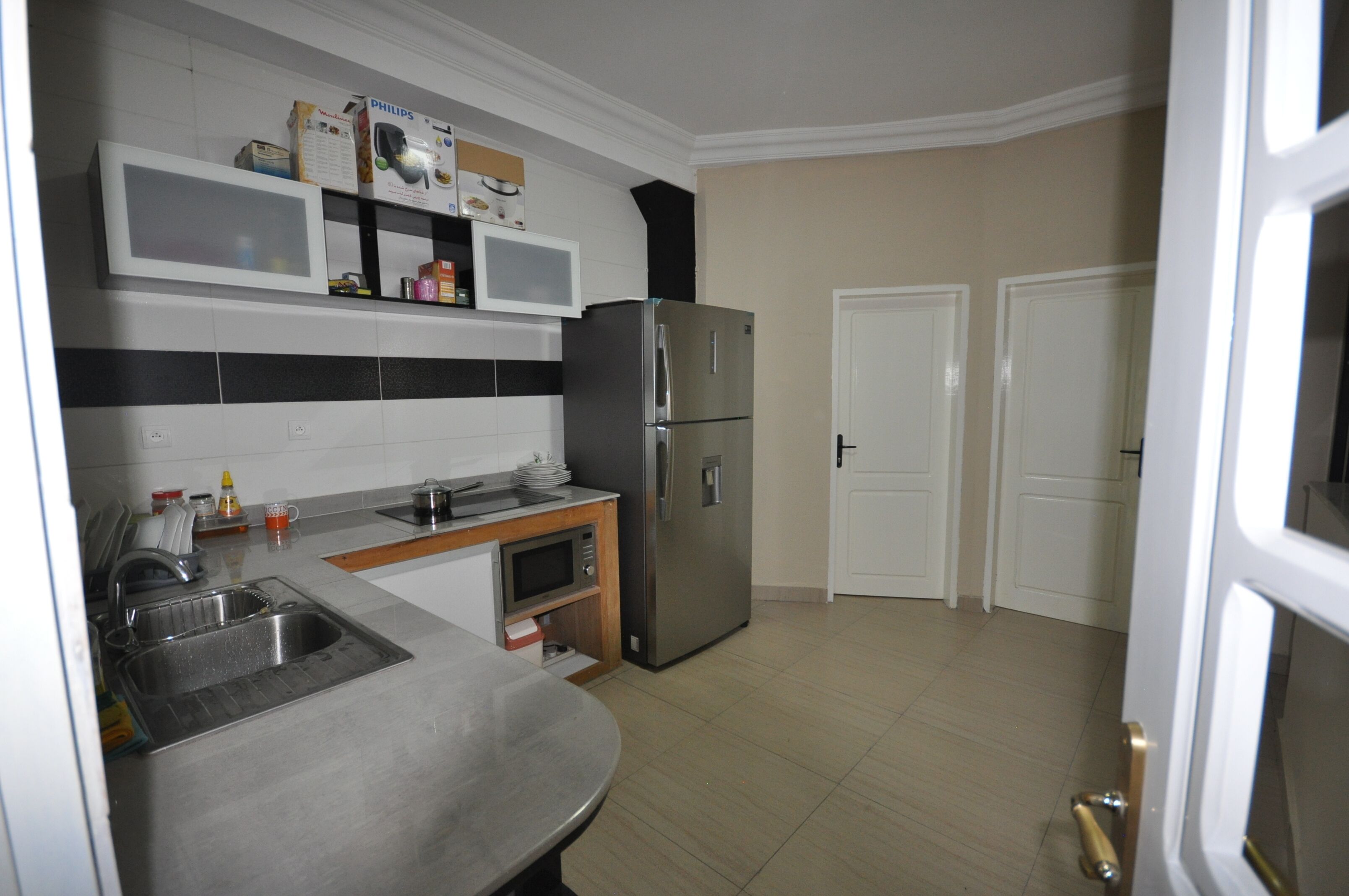 A kitchen with a stainless steel refrigerator, a microwave, and a sink. There are cabinets above the counter and a door to the right.