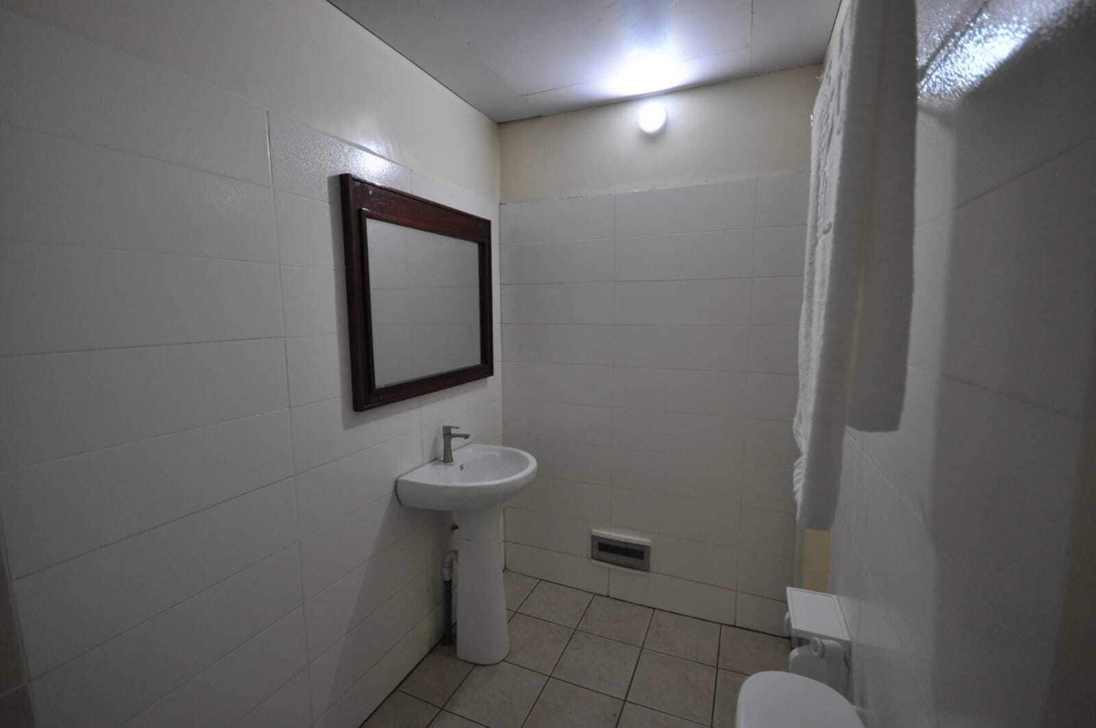 Casa de banho pequena e simples, com lavatório branco, espelho e zona de duche.