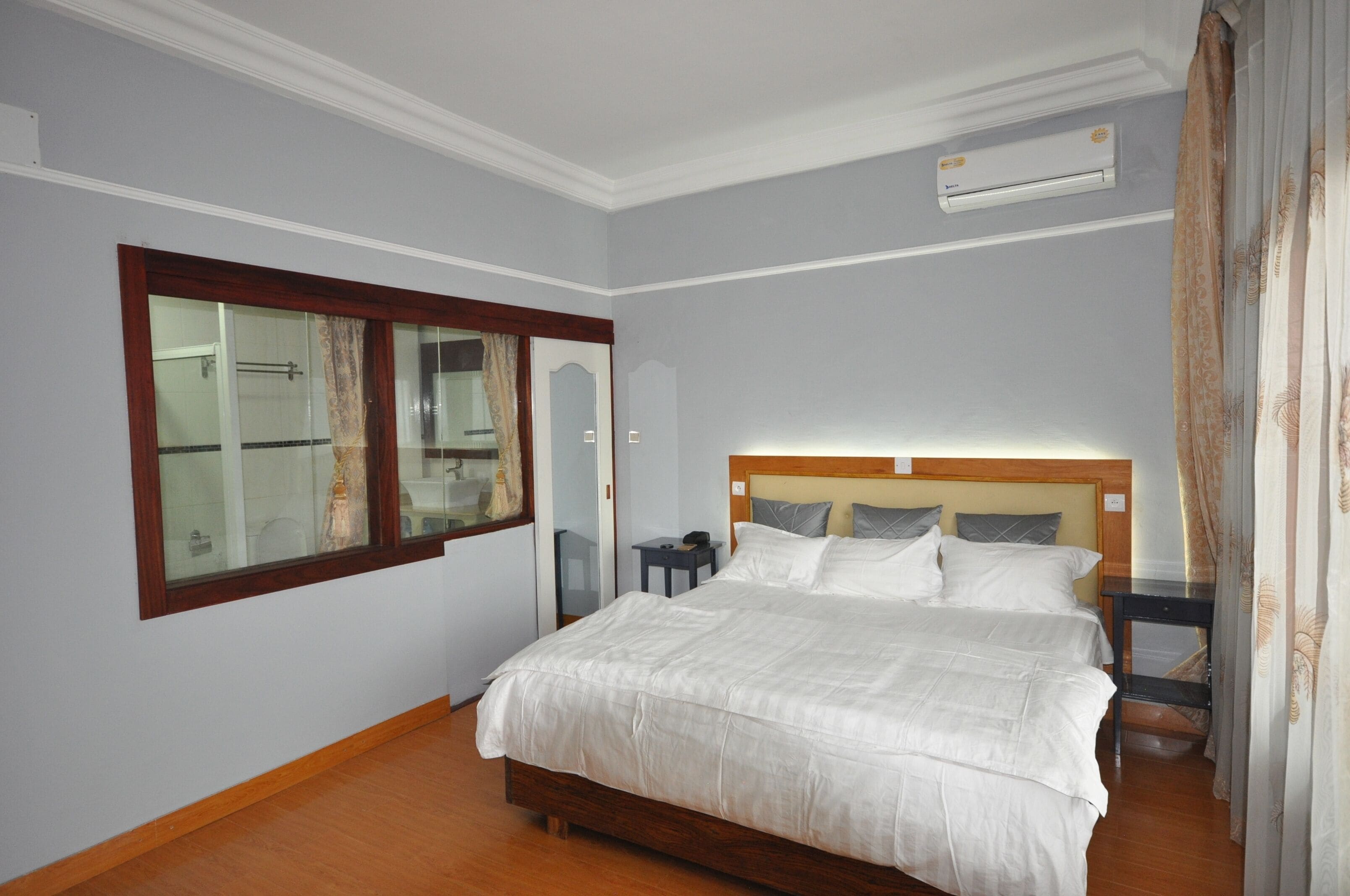 Une chambre avec un grand lit, une table de chevet, un miroir et un appareil de climatisation.