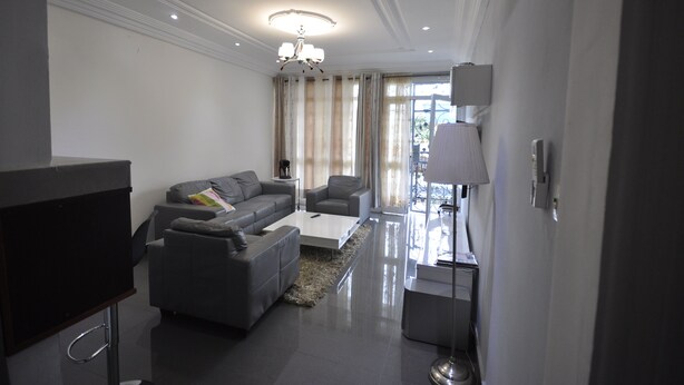 A modern living room with a grey sofa set, a flat-screen TV, and a chandelier. - Line-Residence (Douala)